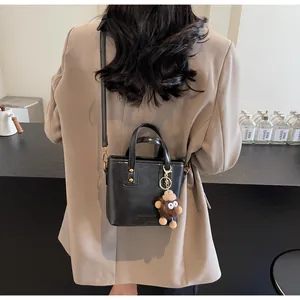Détail du sac bandoulière noir avec finitions dorées et breloque singe en peluche