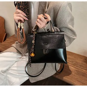 Detail einer schwarzen Handtasche aus Materialmix mit Metallschloss und Anhänger