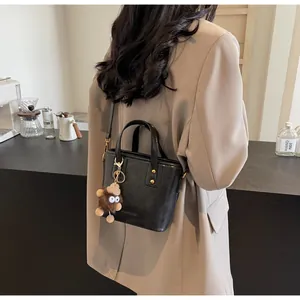 Détail d'un sac seau noir en cuir avec une breloque monstre en peluche marron doux