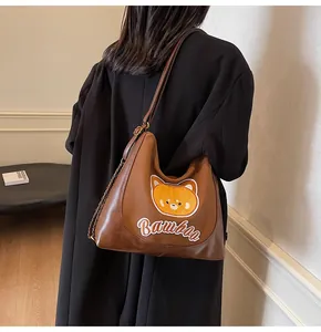Détail d'un sac bandoulière marron avec broderie d'ours et bandoulière en chaîne métal