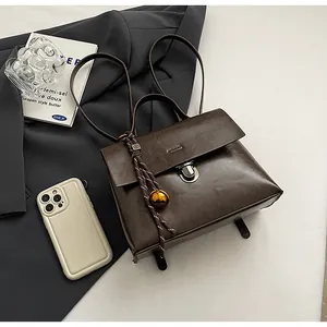 Detail der dunkelbraunen Lederhandtasche mit Silberverschluss auf grauem Anzug