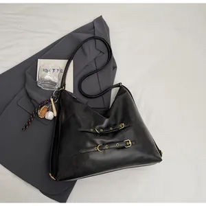 Detail of black faux leather tote bag with metal buckle straps and baseball keychain charm