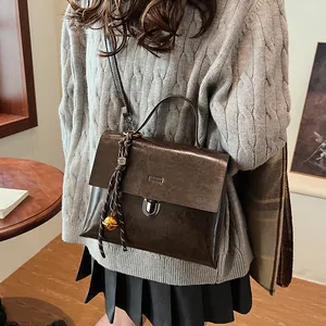 Vintage-Umhängetasche in Dunkelbraun mit gewebtem Glockenanhänger auf grauem Pullover