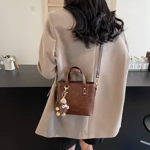 Petit sac rétro marron avec pendentif monstre en peluche porté en bandoulière sur modèle