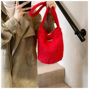 Detail view of a soft red plush bucket bag with a gold plate shown on a stylish model