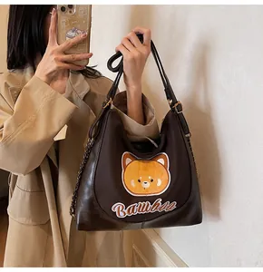 Détail d'un sac cabas en cuir PU marron foncé avec broderie ours orange et bandoulière chaîne