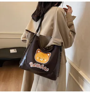 Détail du sac cabas marron foncé avec écusson ours jaune et bandoulière à chaîne