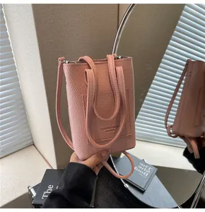 Gros plan du sac bandoulière en cuir grainé rose clair avec poignées et détails du logo