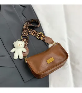 Detail of brown leather crossbody bag with leopard print strap and white plush bear charm
