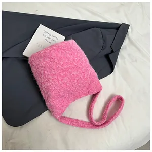 Close-up of bright pink fuzzy knit bucket bag on gray suit and white book backdrop