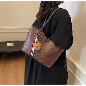 Detail of dark brown leather tote bag with white contrast stitching and plush bear charm