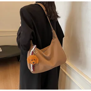 Details der hellbraunen Halbmond-Schultertasche mit Ziernähten und Plüsch-Anhänger