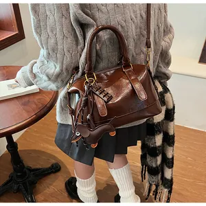 Detail view of dark brown gloss boston bag with dog charm and shoulder strap