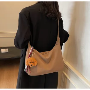 Detail der Hobo-Tasche aus braunem Leder mit Teddy-Anhänger und gewebter Bandverzierung
