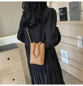 Brown textured leather mini crossbody bag shown on a model in a stylish home setting