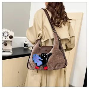 Détail d'un sac en velours marron avec broderie chat noir porté dans un décor d'intérieur