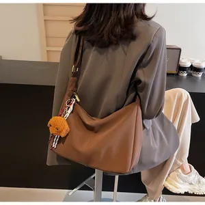 Braune Hobo-Tasche aus Leder mit Bärenanhänger in einer Lifestyle-Café-Umgebung