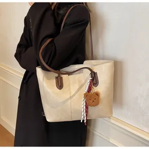 Detail of minimalist cream tote bag with brown straps, cute bear charm and striped scarf