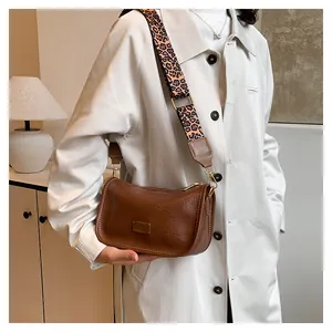 Brown leather Boston bag with leopard print strap shown on a cream winter coat