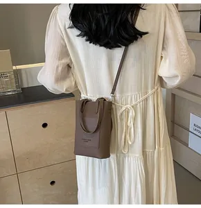 Detailed view of brown lychee leather phone bag worn by model in elegant cream dress
