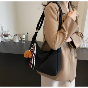 Detail einer schwarzen Nylon-Tasche in Halbmondform mit Teddybär-Anhänger und breitem Gurt