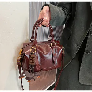 Detail of burgundy glossy leather Boston bag with dog charm and gold hardware accents