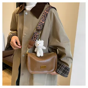 Brown Boston bag with leopard print strap and plush bear charm shown on a trench coat