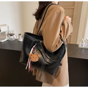 Detail of black tote bag with white stitching and cute brown plush bear charm accessory