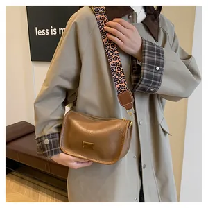 Detail of brown leather bag with leopard print strap and gold metal hardware plaque