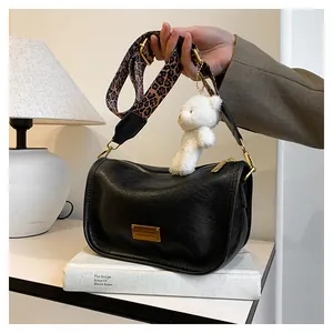 Close-up of black crossbody bag with leopard print strap and cute plush bear charm