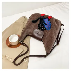 Détail du sac cabas en velours marron avec broderie chat sur literie blanche