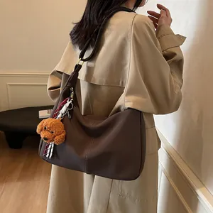 Braune Leder-Tote-Bag mit Teddybär-Anhänger, getragen von Model im beigen Mantel