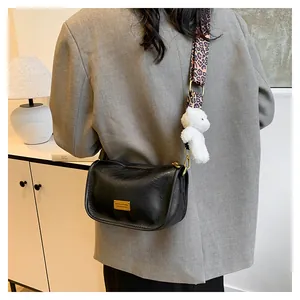 Detail of black Boston bag with leopard strap and plush bear charm on grey blazer