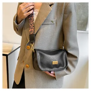 Detail of black faux leather crossbody bag with leopard print strap and gold hardware