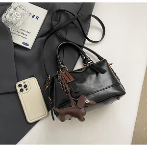 Detail of black glossy leather Boston bag featuring dog charm and chocolate pendant