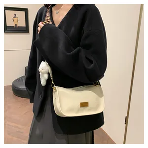 Detail of cream Boston bag with leopard print strap and plush bear charm on model