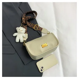 Close-up of cream Boston bag with leopard strap and plush bear charm on grey fabric