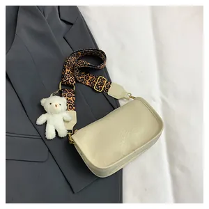 Close-up of beige crossbody bag with leopard print strap and plush bear charm on a suit