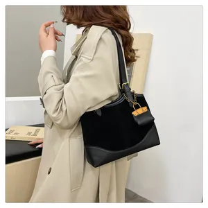 Detail of black tote bag with gold chain and padlock decoration worn by a model in a trench coat