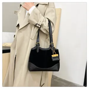 Detail of black bucket bag with gold buckle and mini bag charm on a beige trench coat