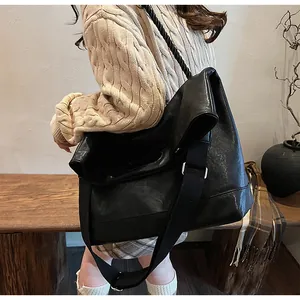 Détail d'un grand sac cabas en cuir souple noir porté par un mannequin en intérieur