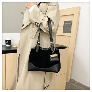 Detail of black bucket bag with gold charms and mixed textures on beige trench coat