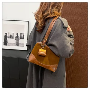 Detailed side view of brown suede bucket bag with leather trim and mini charm accessory