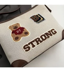Detail of canvas tote featuring teddy bear embroidery and brown leather trim accents