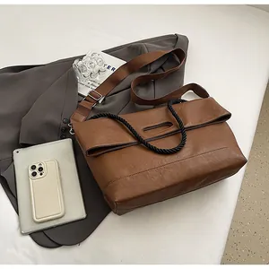 Détail d'un grand cabas en cuir souple marron avec poignée tissée sur une veste grise