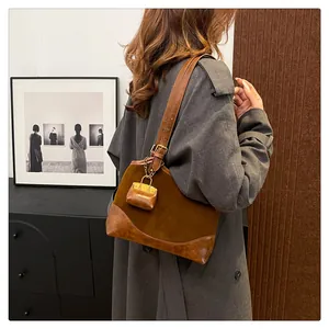 Detail of brown suede bucket bag with leather strap and mini pouch pendant on a model