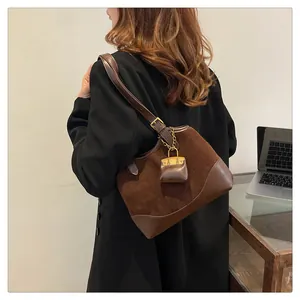 Close-up of brown suede patchwork bucket bag with golden chain charm accessory