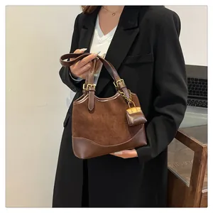 Close-up of brown suede bucket bag with leather stitching and small charm detail