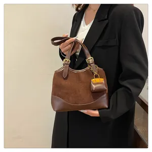 Detail of a brown suede bucket bag with leather patchwork and mini pouch charm on model