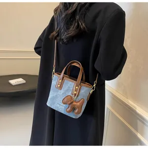Detail der Denim-Beuteltasche mit braunem Lederbesatz und süßem Welpen-Anhänger am Riemen